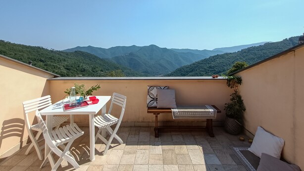 Ein Balkon mit Tisch, Stühlen und einer Bank, mit Blick auf grüne Berge.