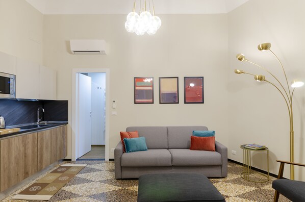 Un salon moderne avec un canapé, une table basse et un lampadaire. Il y a également un coin cuisine équipé d’un four à micro-ondes et d’un évier.