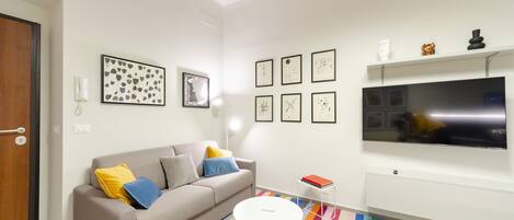 A modern living room with a sofa, colorful rug, and a flat-screen TV mounted on the wall.