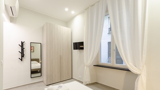Een moderne slaapkamer met een bed, een kledingkast, een televisie en een raam met gordijnen.