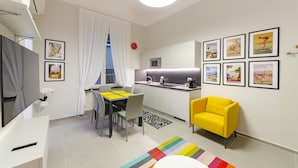 Een knus woongedeelte met een eethoek, een keuken, een gele fauteuil en een flatscreen televisie.