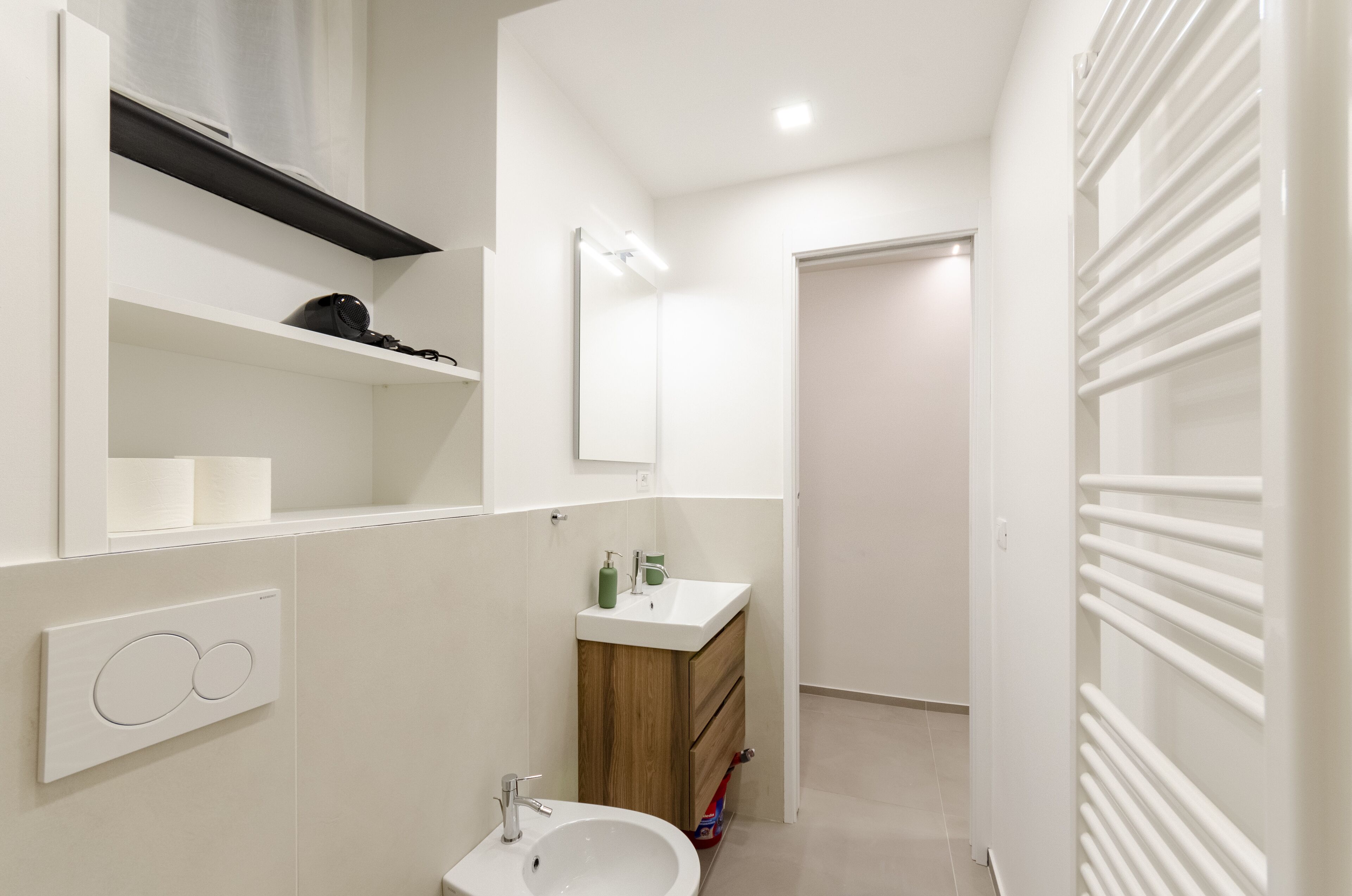 A modern bathroom with a white sink, mirror, and shelves.