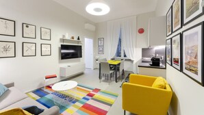 Een moderne woonkamer met een flatscreen televisie, een eethoek met tafel en stoelen, en een keuken met een spoelbak en aanrecht.