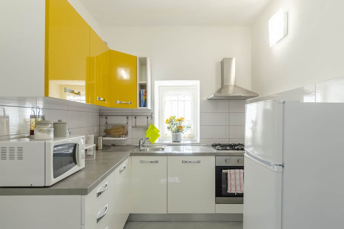 A modern kitchen with white cabinets, a yellow accent wall, a microwave, a sink, and a stove.