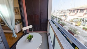 Un balcón con vista a un puerto deportivo, una mesa blanca con una planta en maceta y una puerta cerrada.