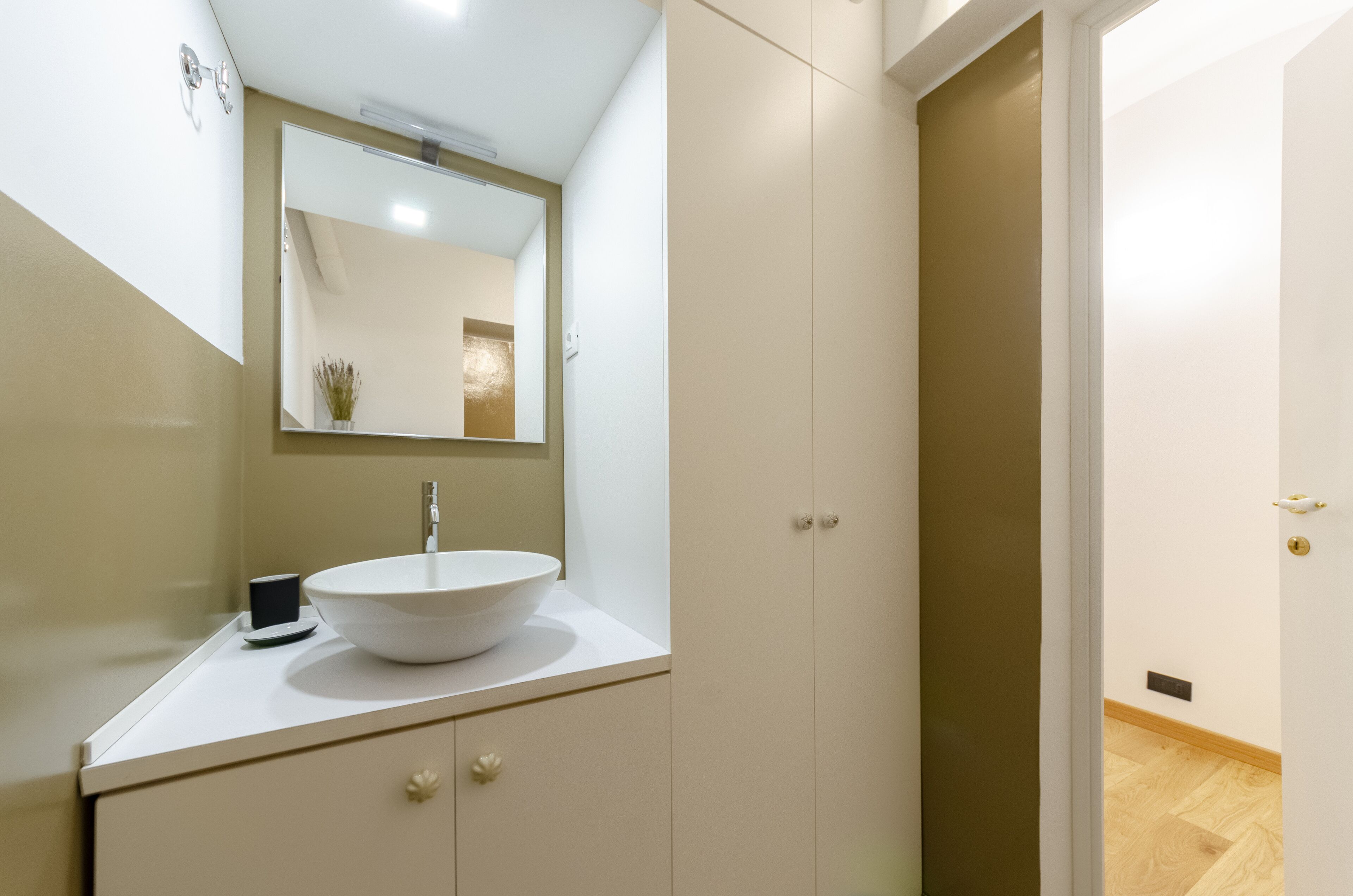 Ein modernes Badezimmer mit einem weißen Waschbecken, einem Spiegel und einem Schrank mit einer kleinen Pflanze.