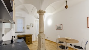 A modern kitchen with a marble countertop, a central column, and a dining area with a round table and chairs. - JOIVY Cute Flat Near The Aquarium (Genoa)