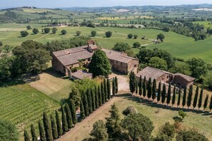 Vista aérea de una finca histórica con varias construcciones, extensos campos verdes y una hilera de cipreses.