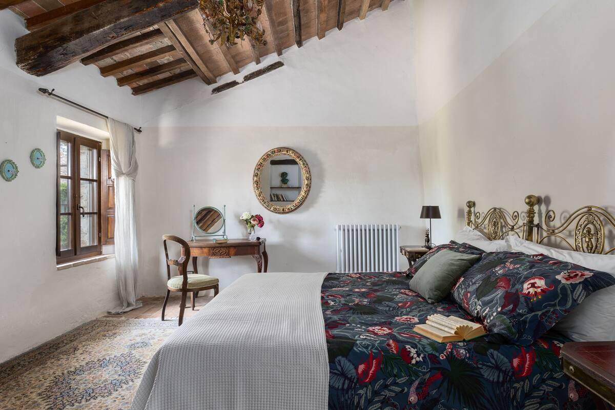 A bedroom with a bed, a desk, a chair, a radiator, and a window.