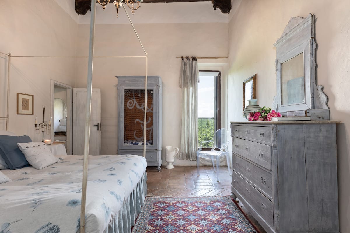 A bedroom with a four-poster bed, a dresser, a chair, and a window with curtains.