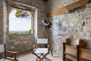 Una habitación rústica con un amplio ventanal arqueado, un sillón de director y un banco de madera.