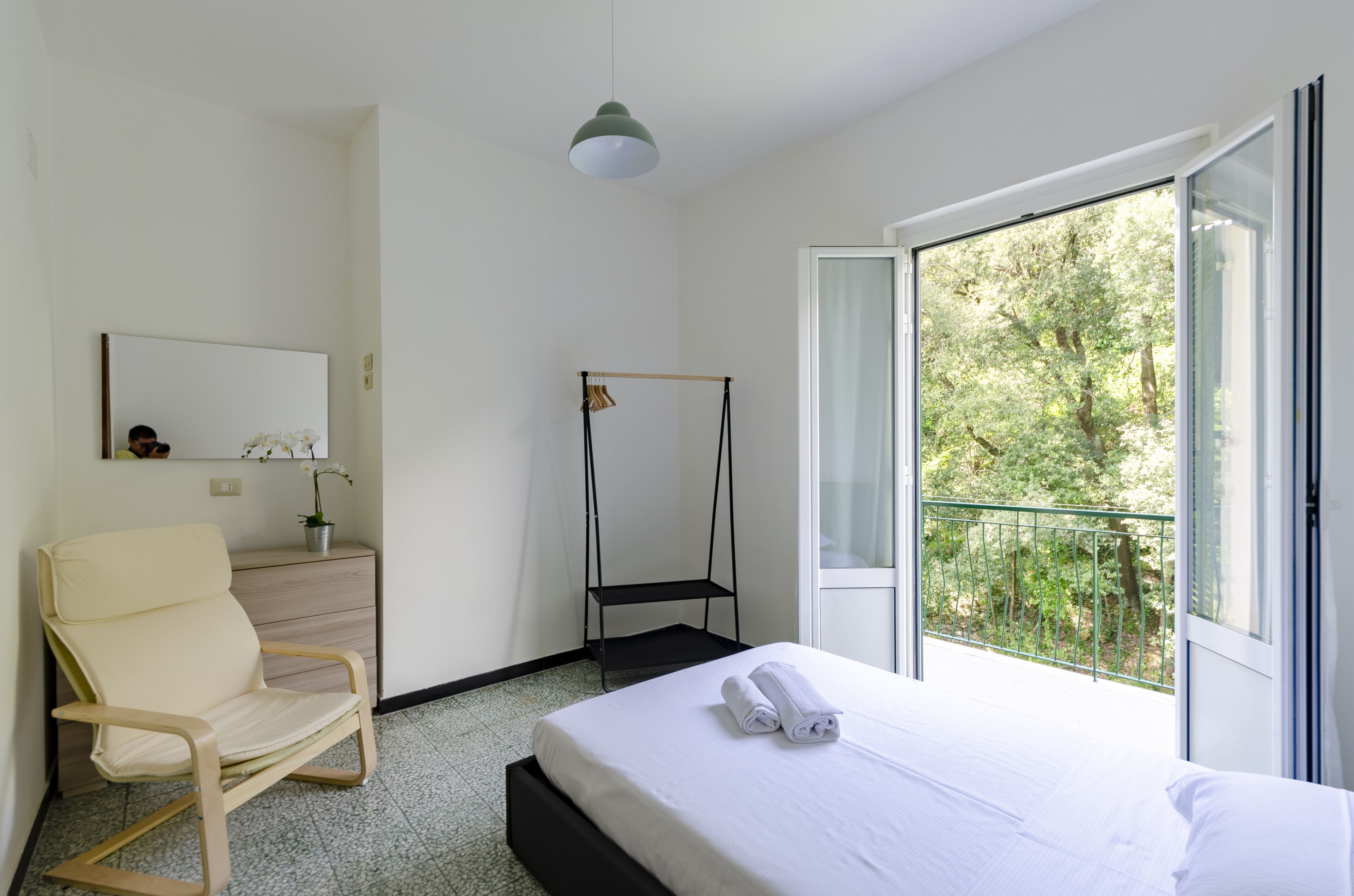 Una camera d'albergo con un letto, una sedia, un tavolino, una poltrona sospesa e un balcone con vista sugli alberi.