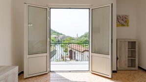 Een kamer met een grote schuifdeur naar een balkon met uitzicht op gebouwen en groen.