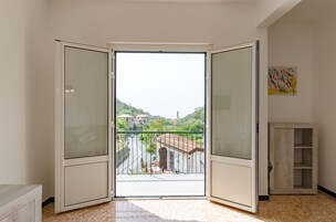Una habitación con un gran ventanal corredero que da a un balcón con vistas a edificios y zonas verdes.