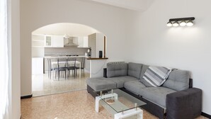 Een moderne woonkamer met een grijze modulaire bank, een glazen salontafel en een eethoek met een witte tafel en stoelen.