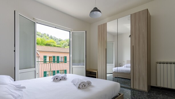 Een hotelkamer met een bed, een kledingkast, een raam met uitzicht op gebouwen, en een balkon.