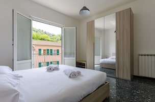 Una habitación de hotel con cama, armario, ventana con vistas a edificios y balcón.