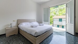 Een slaapkamer met een bed, nachtkastje en uitzicht op een balkon met beplanting.