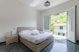 Un dormitorio con cama, mesita de noche y vistas a un balcón con vegetación.