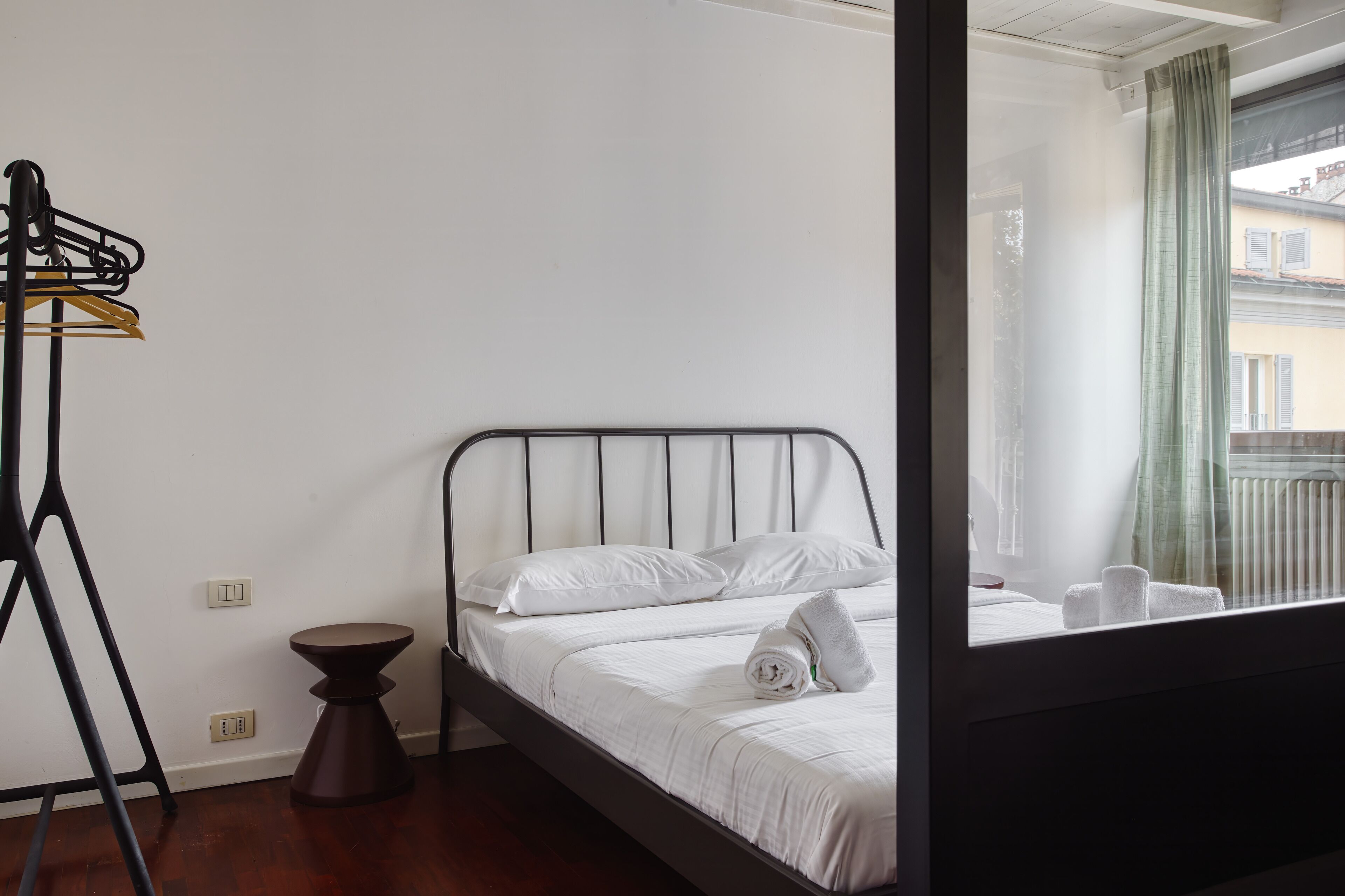 A room with a bed, a small stool, and a metal rack with clothes.