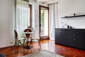 Une cuisine avec une table à manger, des chaises, un meuble noir et une fenêtre avec des rideaux.