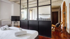 A modern hotel room with a large bed, a television, a desk, and a view of the kitchen through a glass partition. - JOIVY Superb Studio In The Centre Of Milan (Milan)