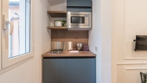 A compact kitchen with a built-in microwave, a gas stove, and a small countertop. - JOIVY Trevi Fountain's relais (Rome)