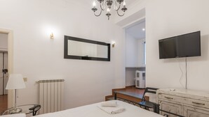 A hotel room with a bed, a TV, a mirror, a radiator, a lamp, and a kitchenette. - JOIVY Trevi Fountain's relais (Rome)
