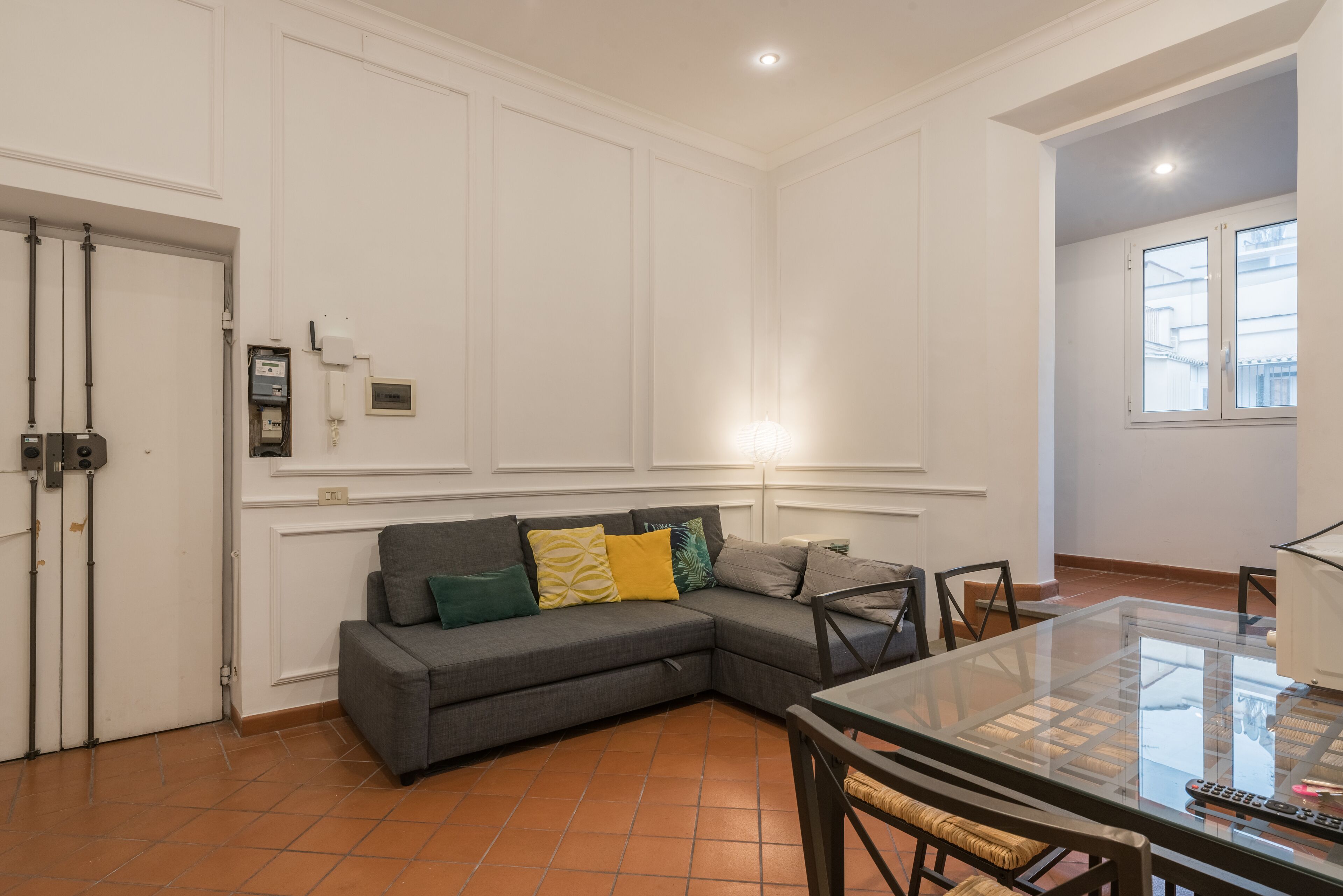 Una sala moderna con un sofá seccional gris, una mesa de centro de vidrio y un comedor con sillas.