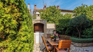 An outdoor patio with a stone table and wooden chairs, surrounded by lush greenery and a stone wall. - Rosy in Rovinj - Istrien / Rosy in Rovinj - Appartement für 4-6 Personen (Rovinj)