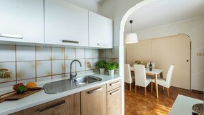 A modern kitchen with white cabinets, a stainless steel sink, and a wooden countertop. There are potted plants on the counter and a dining area with a table and chairs in the background. - Rosy in Rovinj - Istrien / Rosy in Rovinj - Appartement für 4-6 Personen (Rovinj)