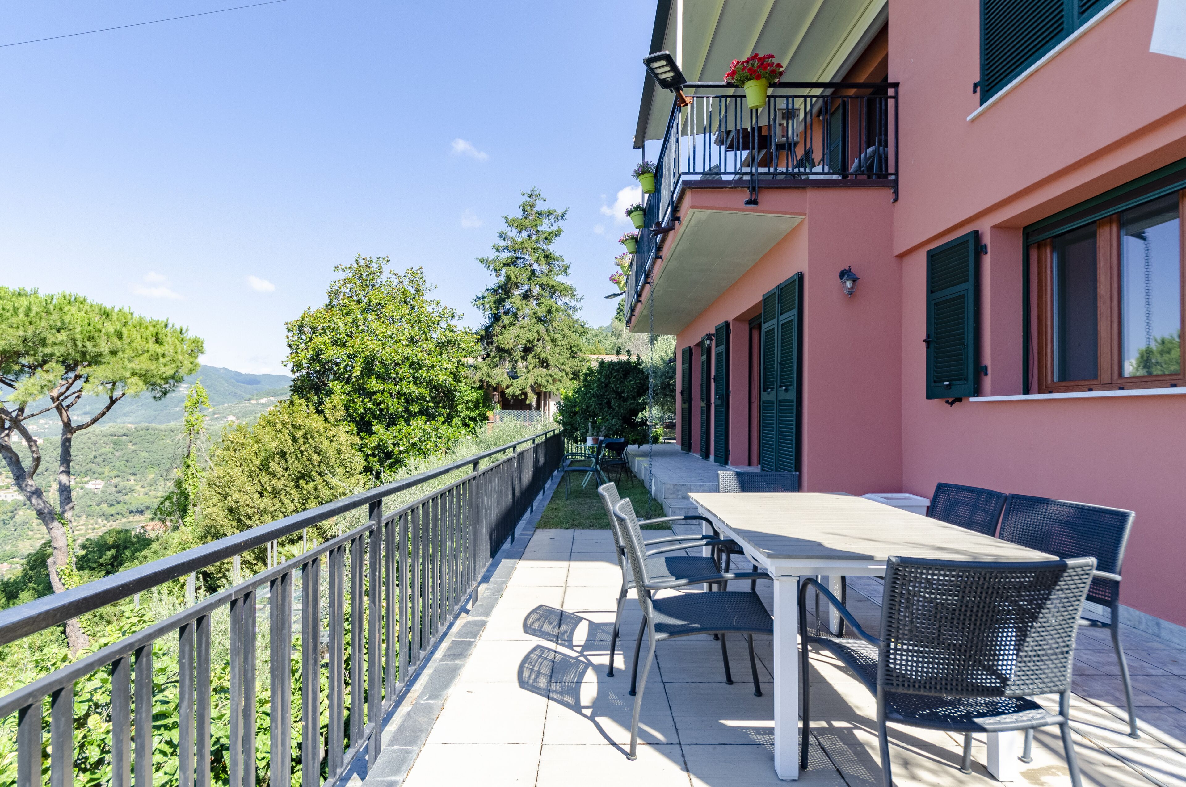 A balcony with a table and chairs, overlooking a scenic view of trees and hills.