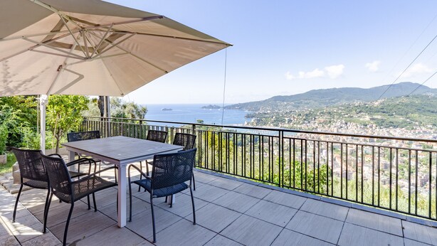 Una terrazza con tavolo e sedie, un ombrellone grande e vista mare e città.