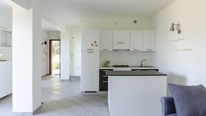 Una cucina moderna con mobili bianchi, un'isola centrale e un divano grigio sullo sfondo.