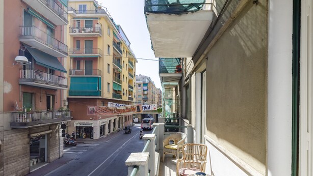 A balcony with wicker furniture and a view of a street with buildings and shops.