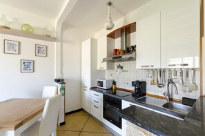 A modern kitchen with white cabinets, a black countertop, and a dining area with a wooden table and white chairs.
