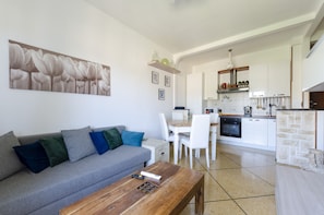 A modern kitchen with white cabinets, a central island, and a dining area with white chairs.