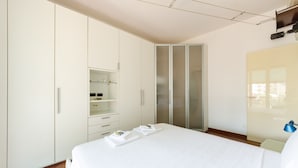 Ein modernes Hotelzimmer mit einem großen Bett, einem weißen Schrank und einem Glastüren-Kleiderschrank.