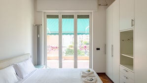 Ein Hotelzimmer mit Bett, Schrank und einem Balkon mit Blick auf Gebäude und Blumen.