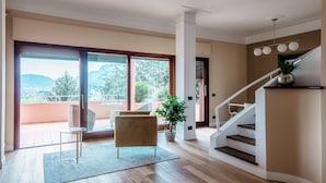 Amplia sala de estar con puerta corrediza de vidrio que da a un balcón, una escalera y una planta en maceta.