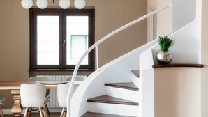 Un interior moderno con una escalera, zona de comedor y una ventana con persianas.
