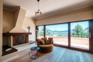 A modern living room with a fireplace, a round sofa, and a large window offering a view of the outdoors.