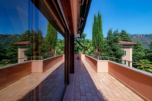 A balcony with a view of a mountainous landscape, featuring terraced gardens and tall trees.