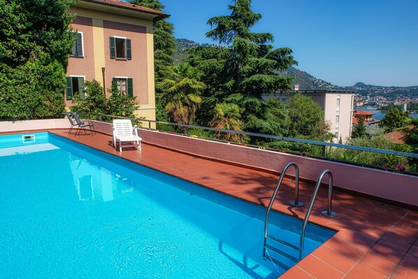A rooftop pool with clear blue water, surrounded by a red-tiled deck and a metal ladder.