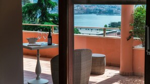 Un balcon avec une table, deux chaises et une bouteille de vin, donnant sur une étendue d’eau et un pont.