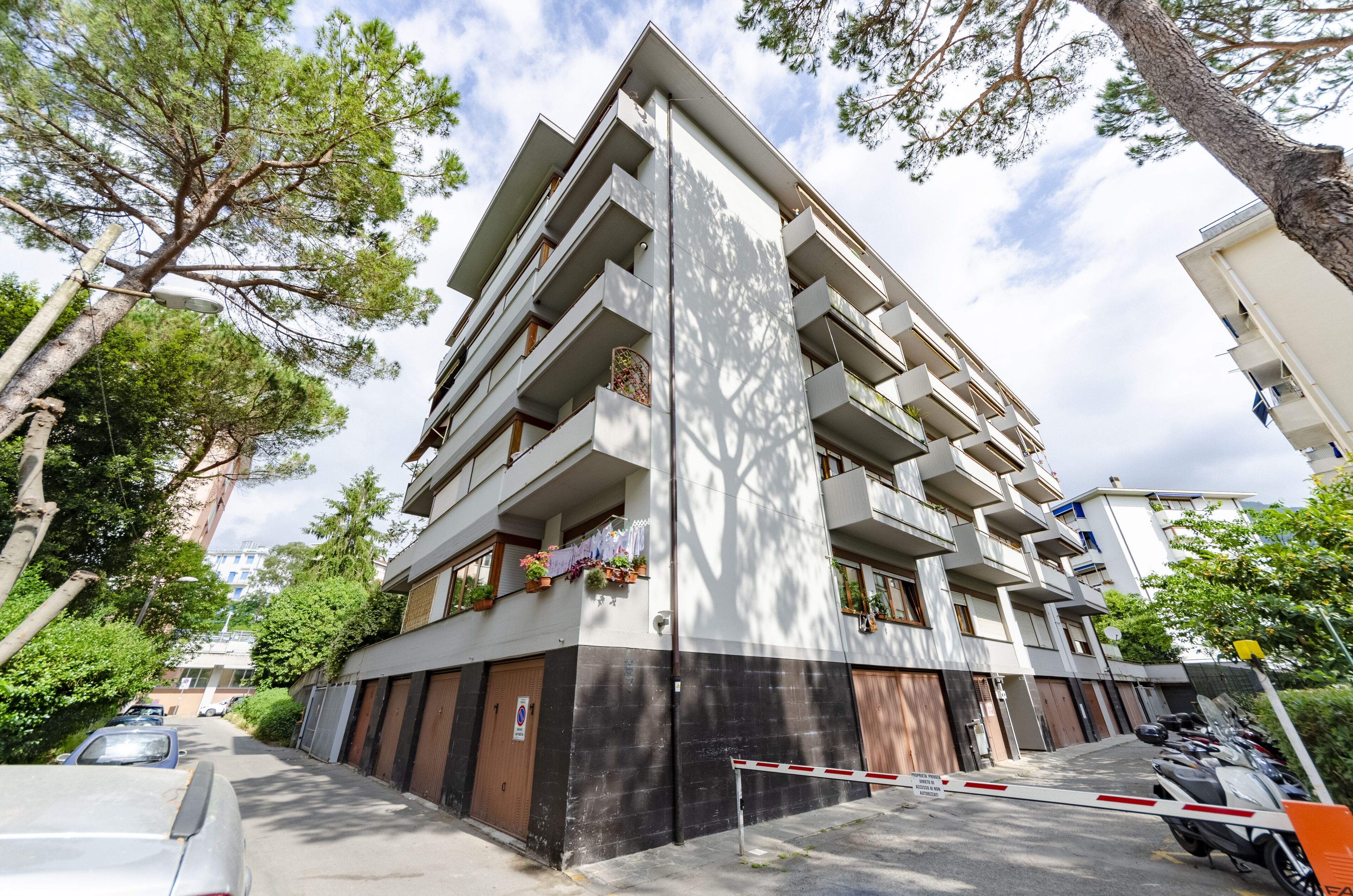 Un edificio residencial de varios pisos con balcones, una entrada con reja y vehículos estacionados.