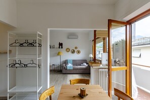 Una habitación con una mesa de comedor, sillas, un sofá, un perchero y una ventana con vistas a edificios.