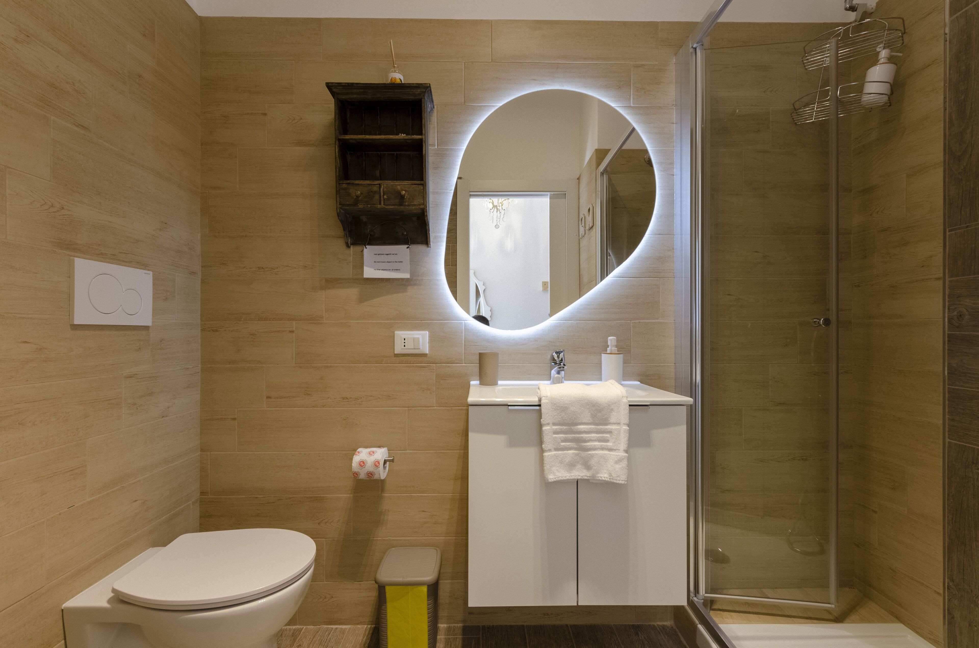 Un baño moderno con suelo de madera, inodoro, lavabo con toalla y cabina de ducha de cristal.