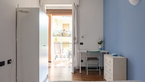A room with a desk, chair, and dresser, leading to an open balcony with outdoor furniture.
