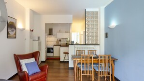 A compact living space with a dining area, kitchen, and a red leather chair with a blue pillow.